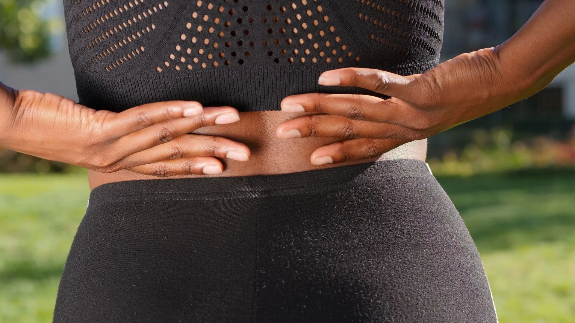 Close crop of a person standing outdoors with both hands pressed to their lower back