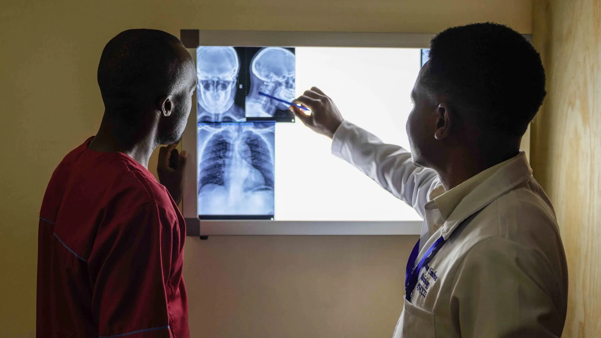 A clinician and a patient standing together reviewing X-ray images on a lit screen