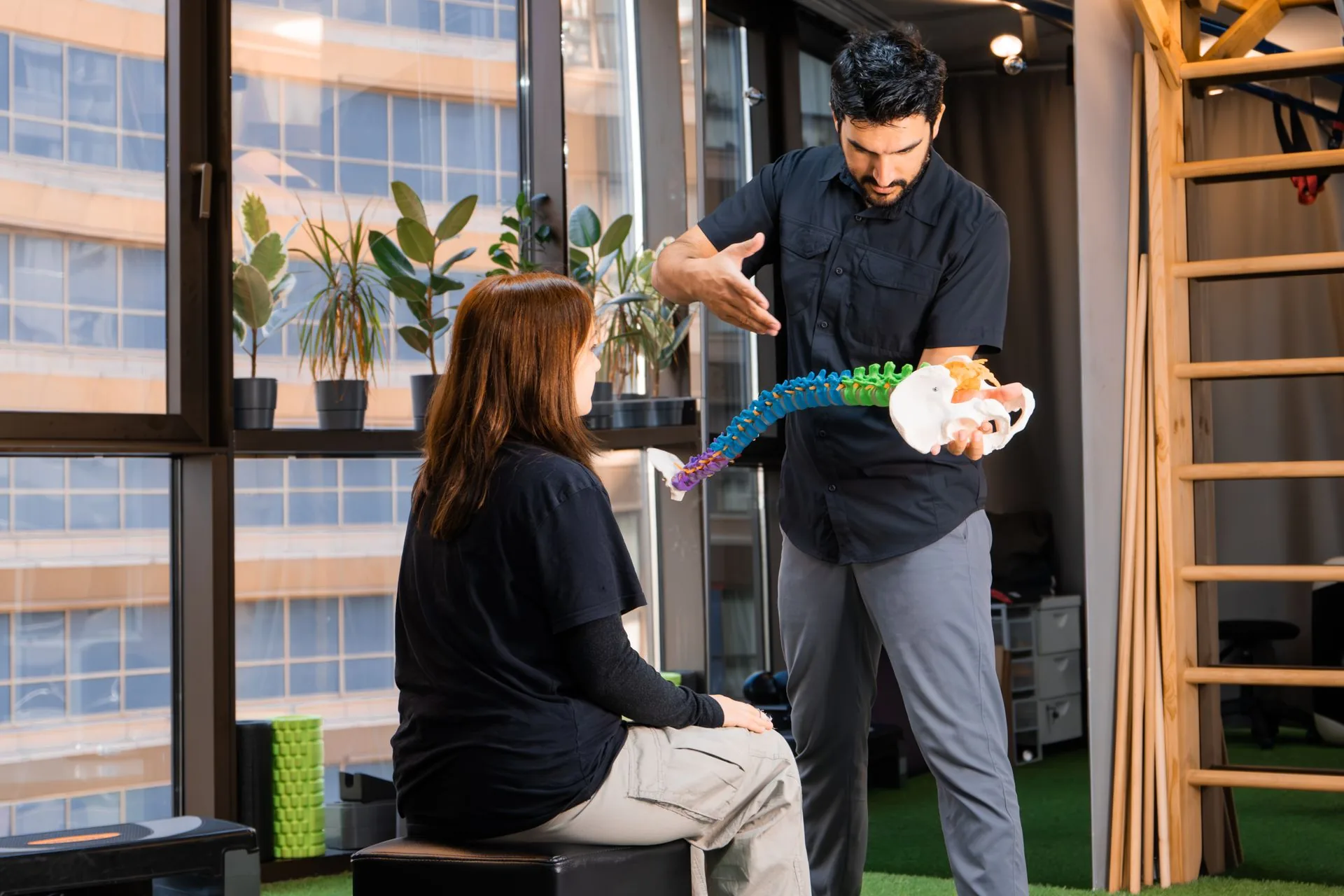 A clinician holding a flexible model of the spine and explaining it to a seated patient
