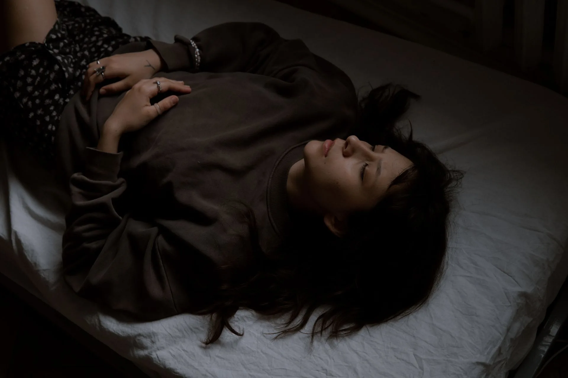 A woman lying on a bed in a darkened room with her eyes closed