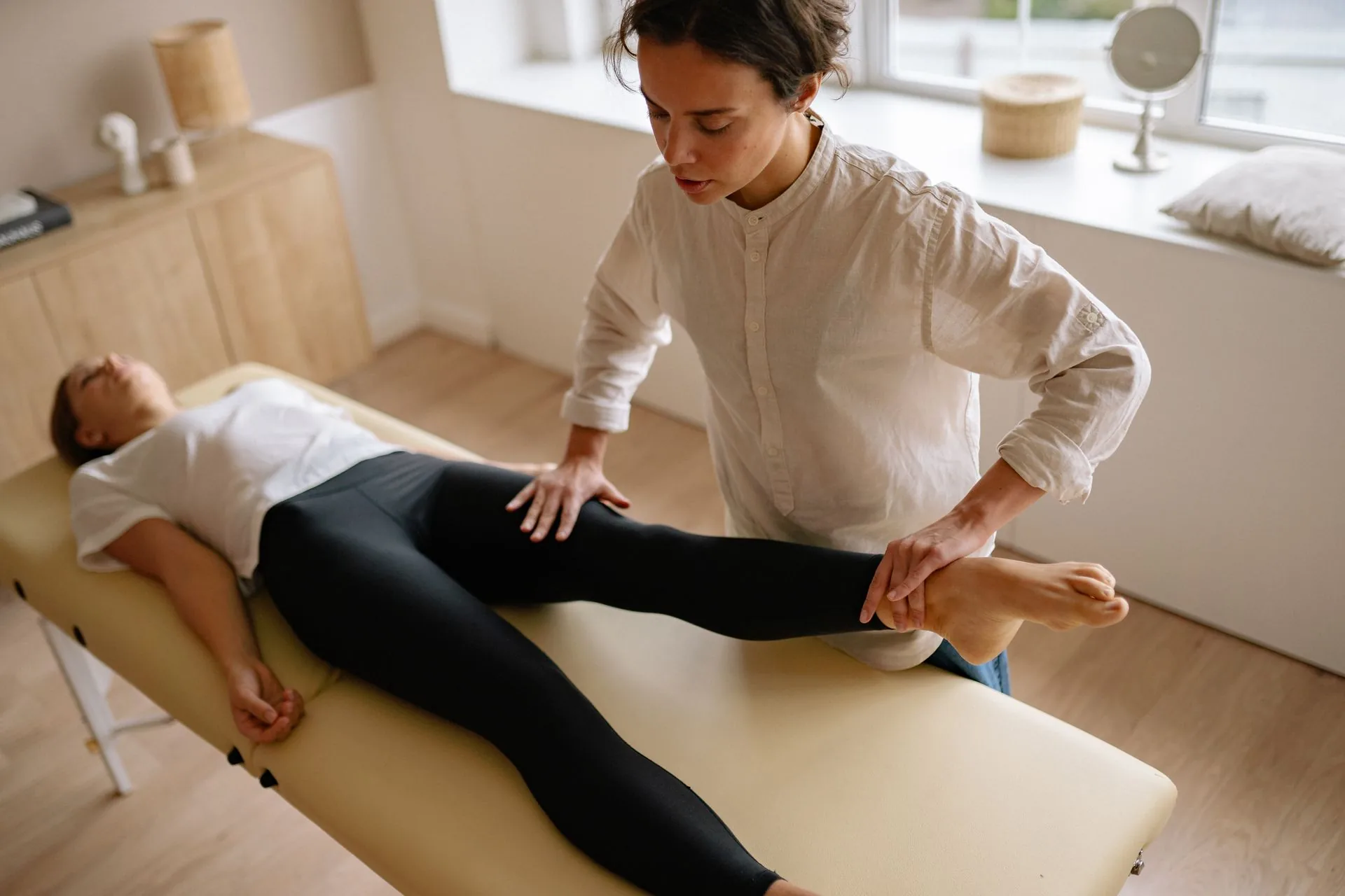A therapist raising a reclining patient's straight leg during a leg-pain examination