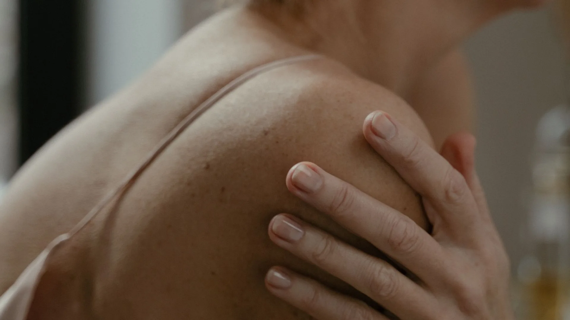 A woman reaching across to hold the top of her opposite shoulder in soft light