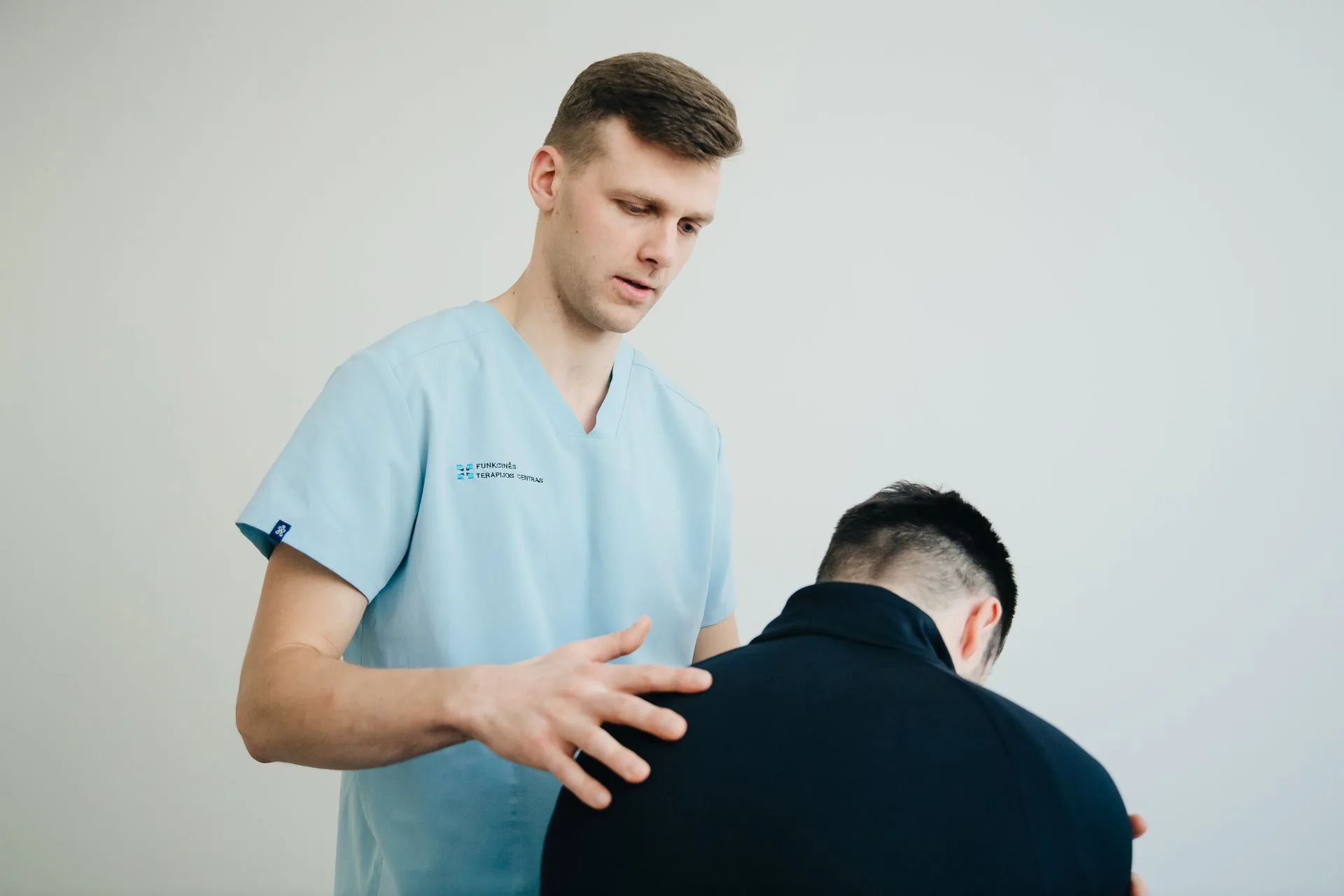 A clinician in scrubs assessing the back of a seated patient leaning forward
