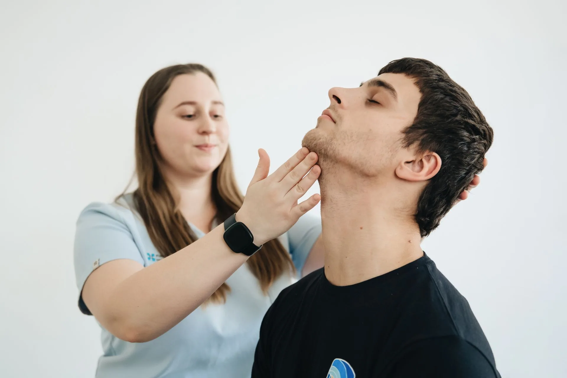 A clinician supporting and assessing a seated patient's neck
