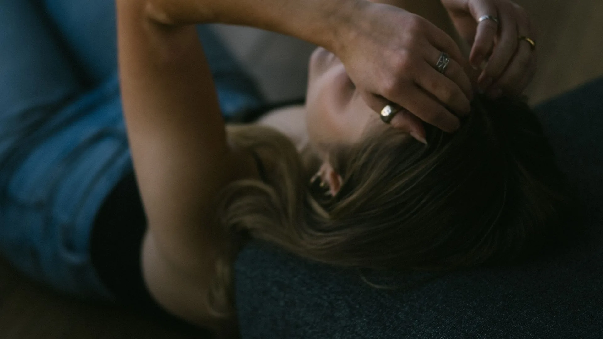 A woman lying down in a dim room with a hand resting against the back of her head
