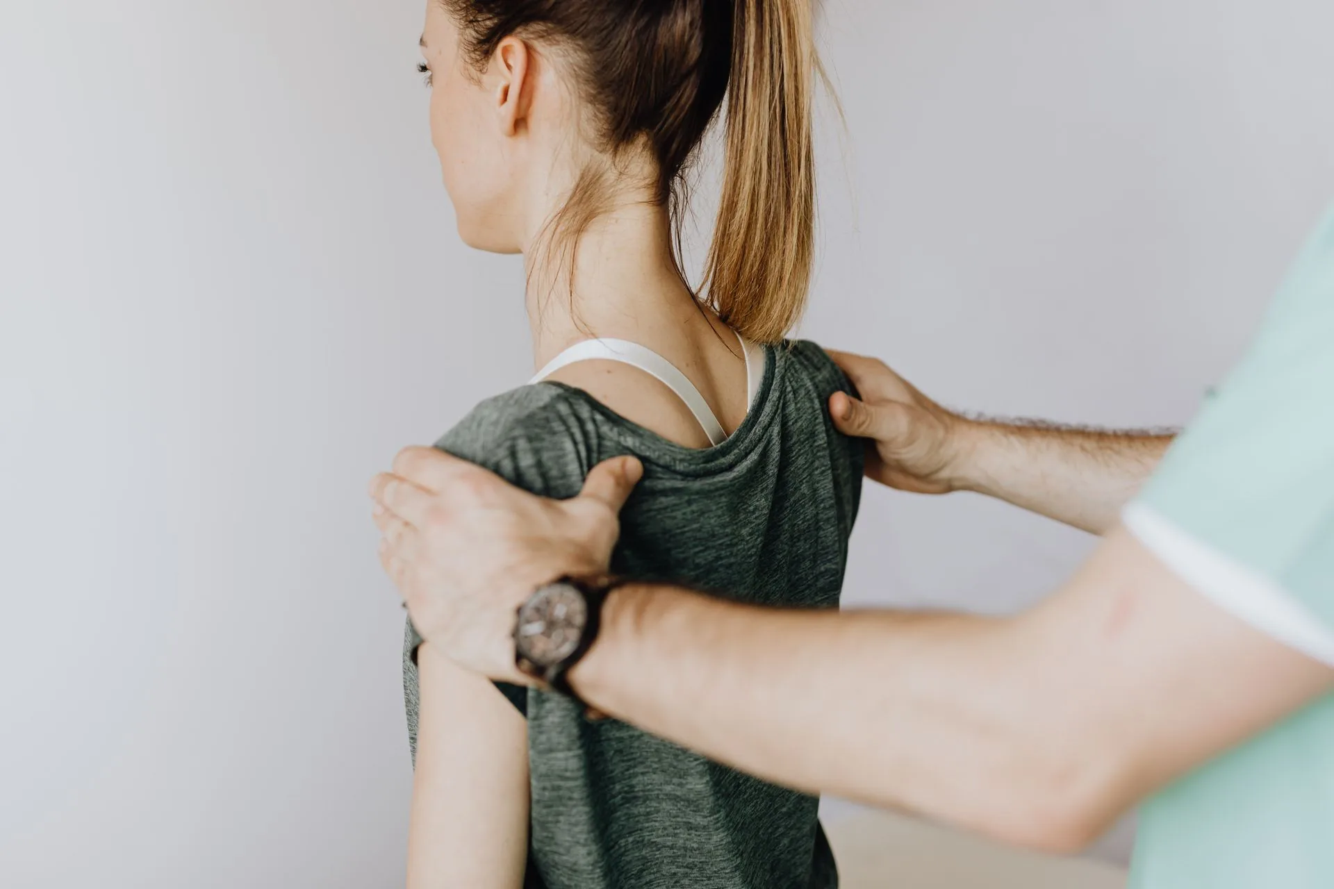 A clinician standing behind a seated patient, both hands assessing the shoulder joint